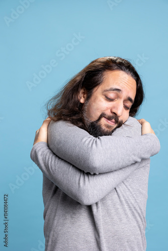 Happy person feeling fulfilled and embracing himself as a form of self love, showing self appreciation and a powerful personality against blue background. Young adult relaxed and confident. photo