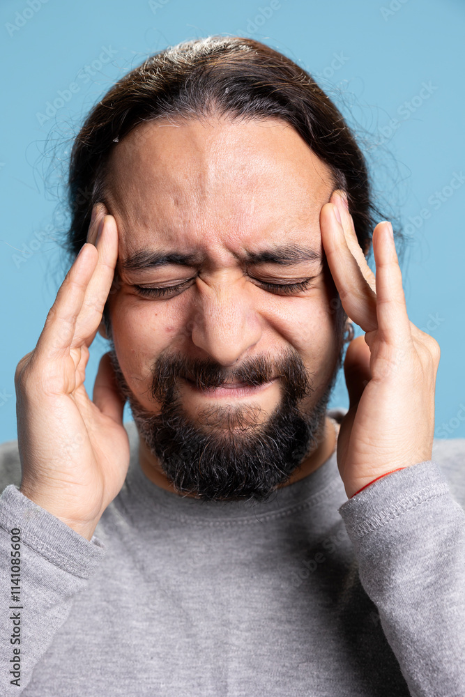 Stressed overwhelmed adult dealing with a headache against blue background, rubbing his temples and trying to relieve pain due to burnout or anxiety. Young guy being sick with a migraine, fatigue. Stressed overwhelmed adult dealing with a headache against blue background, rubbing his temples and trying to relieve pain due to burnout or anxiety. Young guy being sick with a migraine, fatigue.