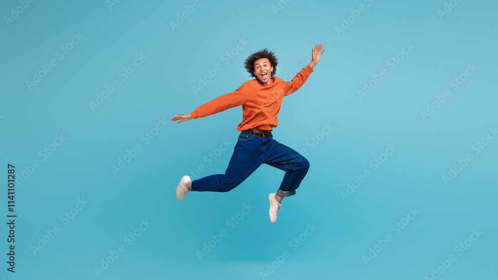 A young African American man with curly hair leaps in excitement, showcasing a fun and carefree moment. Dressed in a bright orange sweater and blue jeans, he embodies a lively lifestyle. A young African American man with curly hair leaps in excitement, showcasing a fun and carefree moment. Dressed in a bright orange sweater and blue jeans, he embodies a lively lifestyle.