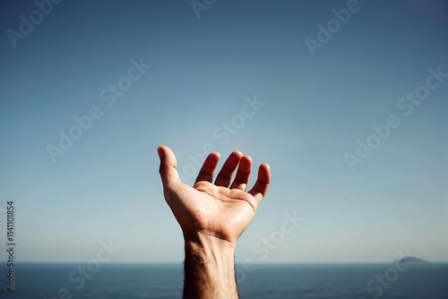 Hand reaching towards the clear sky over the calm sea in a tranquil setting