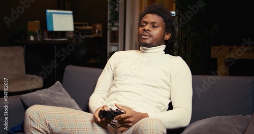 African american man plays intense online videogame, spamming attack buttons on controller. Gamer participating in esports tournament, sitting on couch and playing on gaming console photo