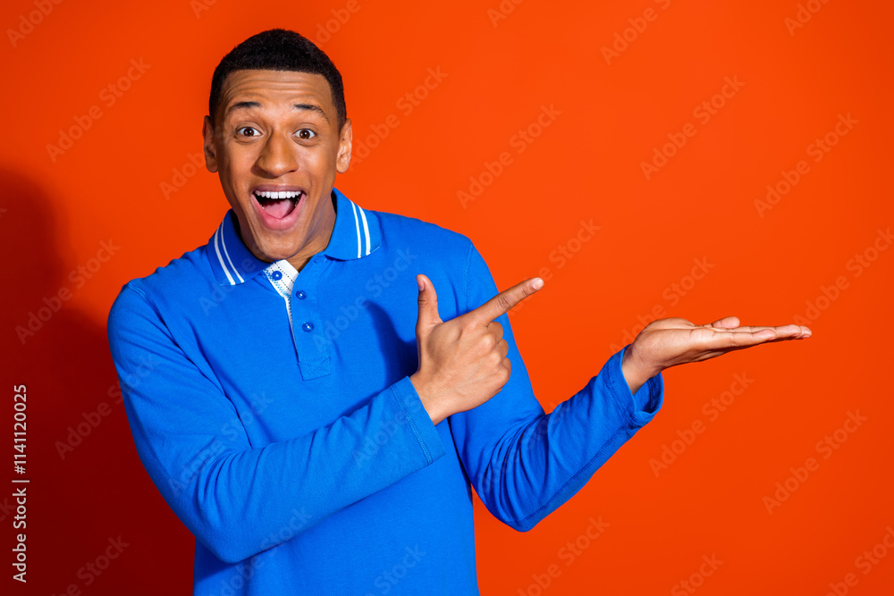 Smiling young man in blue shirt pointing with excitement on orange background Smiling young man in blue shirt pointing with excitement on orange background