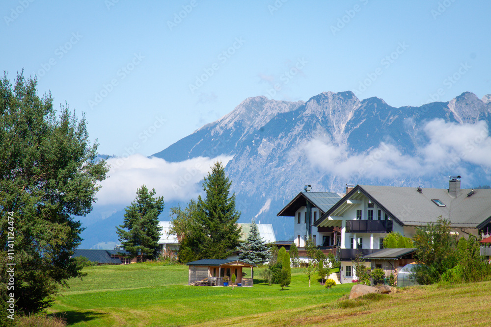 Alpine Village with Houses Nestled Below Mountain Range and Low-Hanging Clouds Alpine Village with Houses Nestled Below Mountain Range and Low-Hanging Clouds