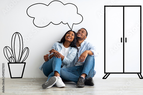 фотографія Dreaming african american spouses imagining interior of their new flat, sitting on floor near wall with doodle drawings and embracing