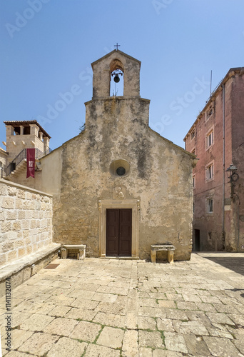 Korcula, Croatia - June 30, 2024: Church of St. Peter front facade with short bell tower behind small square under blue sky