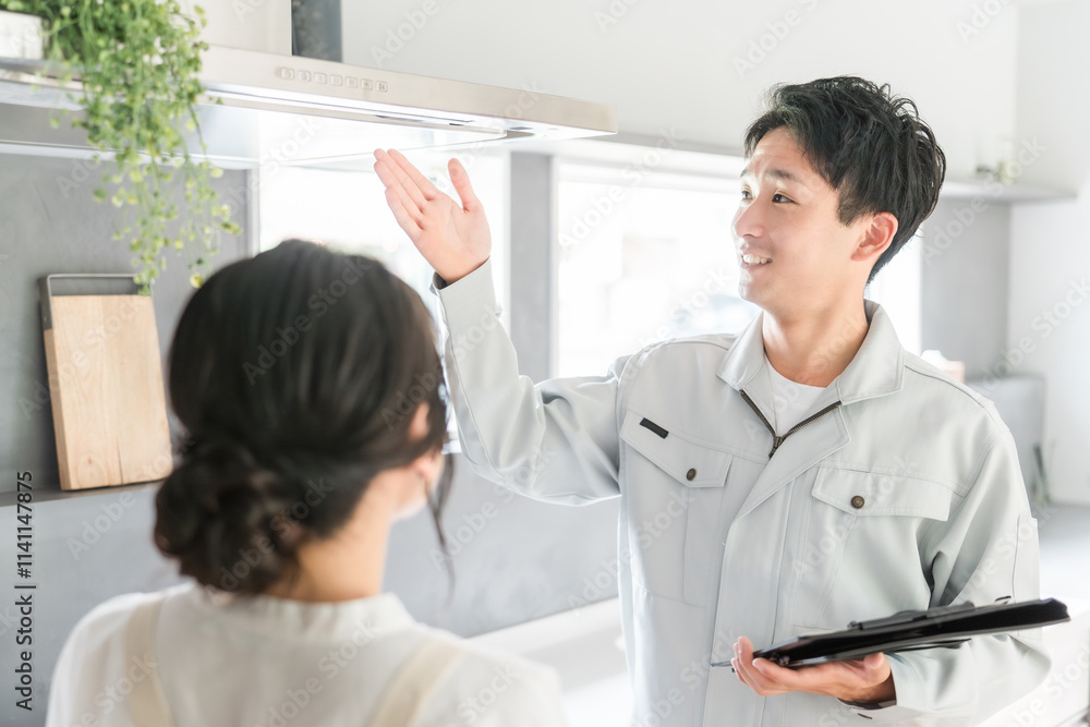 Obraz premium 換気扇・レンジフードの説明を受ける主婦の女性と工務店・設備屋・電気工事士・業者の作業着姿の男性