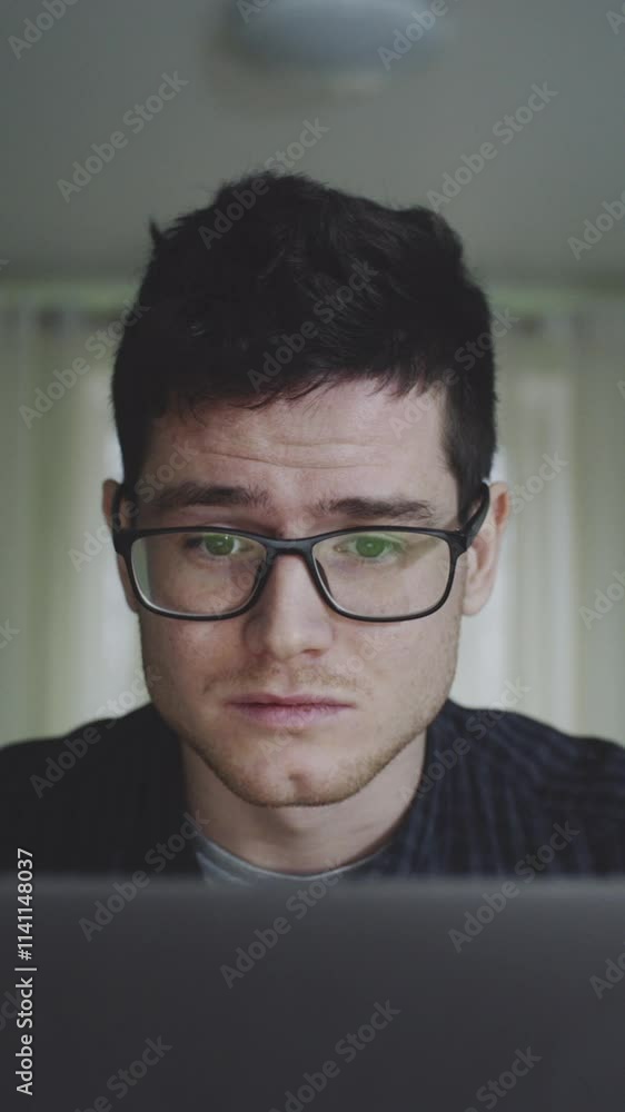 Portrait of millenial freelancer sitting in front of computer at home. Young male working remotely immersing in work in laptop, adjusting glasses. Concept of technology, distant. Portrait of millenial freelancer sitting in front of computer at home. Young male working remotely immersing in work in laptop, adjusting glasses. Concept of technology, distant.