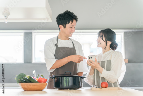 スマホを見ながらキッチンで料理を作る夫婦（レシピサイト・レシピアプリ） 