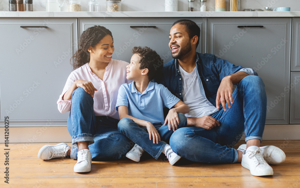 A loving African American family sits on the kitchen floor, sharing laughter and affection. The father, mother, and son engage in a joyful moment, highlighting the warmth of home life. A loving African American family sits on the kitchen floor, sharing laughter and affection. The father, mother, and son engage in a joyful moment, highlighting the warmth of home life.
