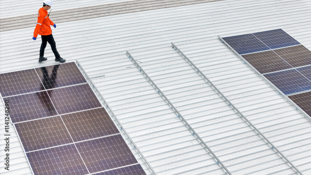 Aerial view of a rooftop with solar panels, showing a technician in safety gear performing maintenance. The scene highlights renewable energy, solar technology, and sustainable infrastructure. Aerial view of a rooftop with solar panels, showing a technician in safety gear performing maintenance. The scene highlights renewable energy, solar technology, and sustainable infrastructure.