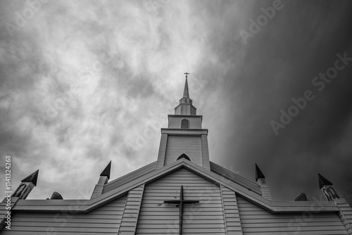 Church steeple with a cross on top rises against a dramatic, cloudy sky photo