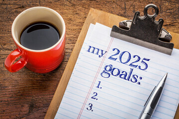 my 2025 goals list on clipboard and coffee against grunge wood desk, setting New Year goals and resolutions
