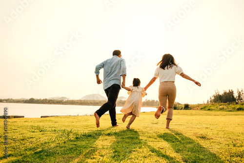 Asian family having fun and enjoying the nature, holding hands running and playing together in a green garden on a sunny day, happy family day