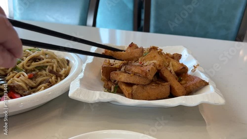 Diner's Delight: Man Using Chopsticks to Savor Fried Tofu at Restaurant