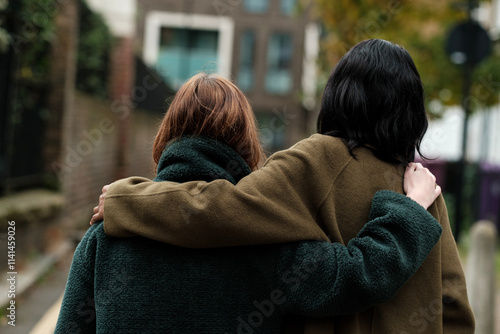 Two friends walking together embracing each other with arms over shoulders