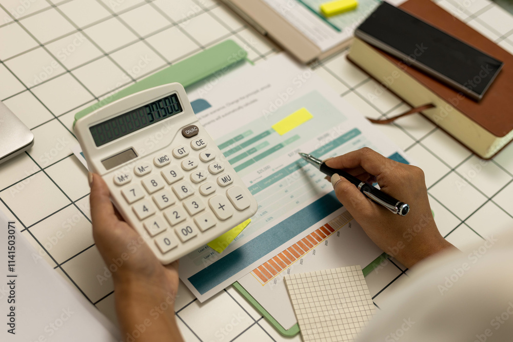 A person is using a calculator to add up numbers on a piece of paper. The paper has a budget and a graph on it