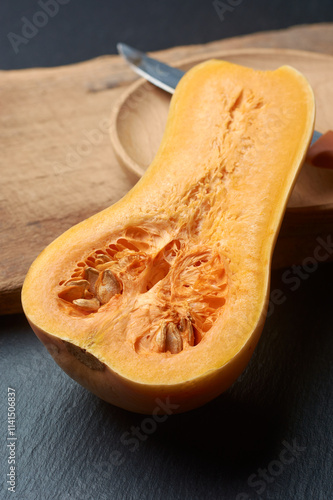 butternut squash cut in half revealing vibrant orange flesh and seeds on cutting board with knife and wooden bowl in background, soft focus with copy space photo