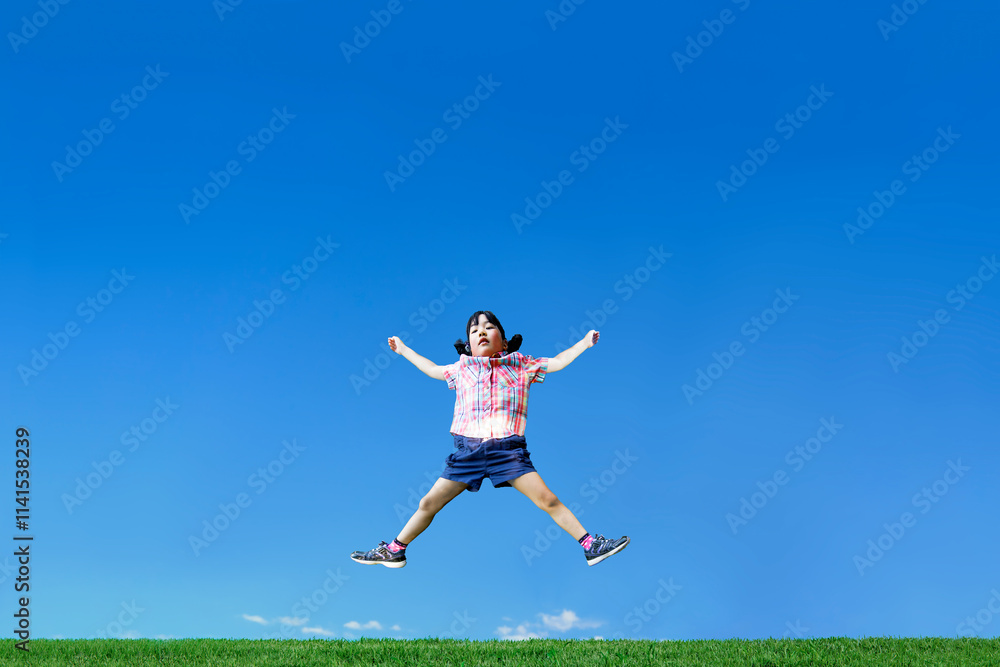 青空を背景に手足を広げジャンプをする幼い女の子1人 青空を背景に手足を広げジャンプをする幼い女の子1人