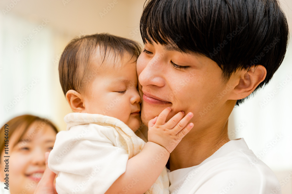 0歳児の赤ちゃんを抱っこする30代の父親の男性と背後の母親