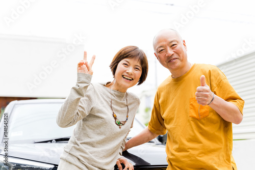 ドライブ前に車の前でピースサインをする50代から60代の仲の良い老夫婦3人 photo