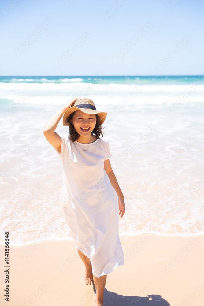 ビーチで帽子を押さえて歩いている笑顔の女性 ビーチで帽子を押さえて歩いている笑顔の女性