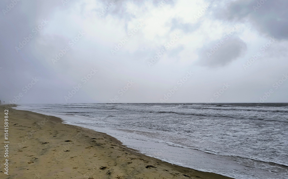 Obraz premium A peaceful beachfront scene featuring gentle waves meeting the sandy shore under an overcast sky. Captures an atmosphere of tranquility, solitude, and the beauty of natural coastal landscapes