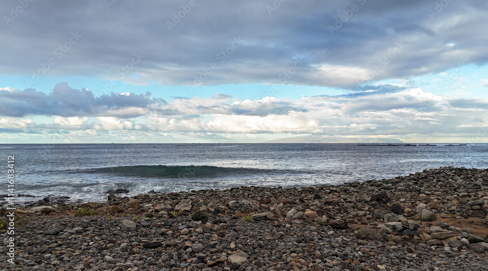 Pebble sea beach in south of Tenerife in the morning with cloudy sky, horizon over water, profile of the island La Gomera Pebble sea beach in south of Tenerife in the morning with cloudy sky, horizon over water, profile of the island La Gomera