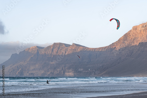 Kite surfer rides across waves at beach near the mountains in Famara, Lanzarote