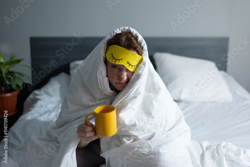 Schilderij op canvas unhappy about waking up early in the morning, a woman sits in bed wrapped in a c