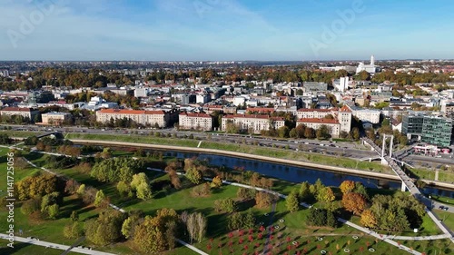 Kaunas cityscape, showcasing the Nemunas river winding through the city center, the Simonas Daukantas bridge and the autumn foliage adorning the parks along its banks, Lithuania, drone orbiting photo