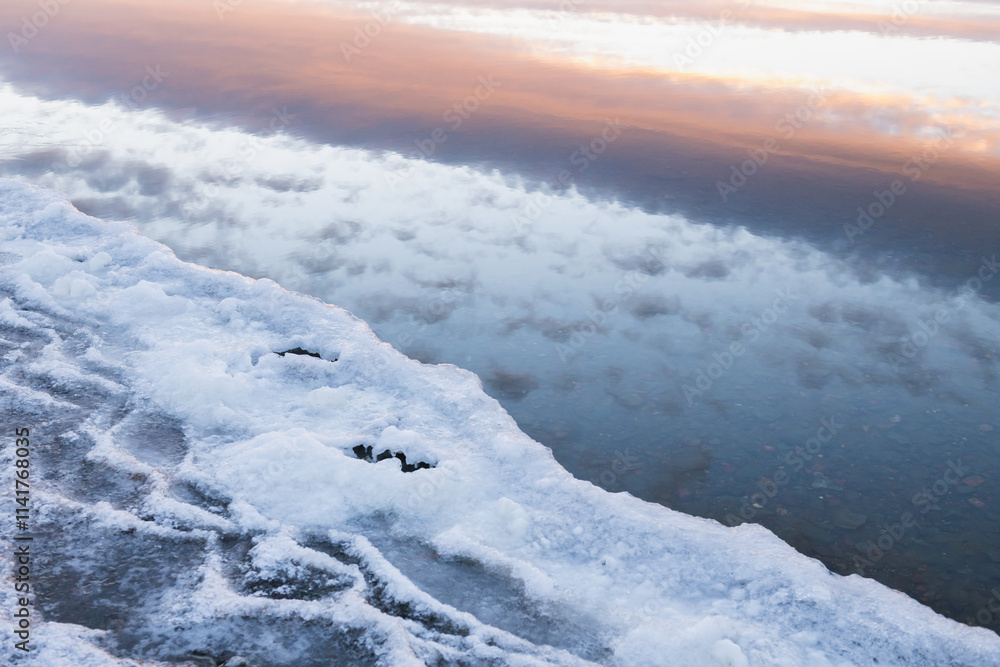 Ice on the shore of lake in winter. Clouds and sky are reflected in the water at sunset Ice on the shore of lake in winter. Clouds and sky are reflected in the water at sunset