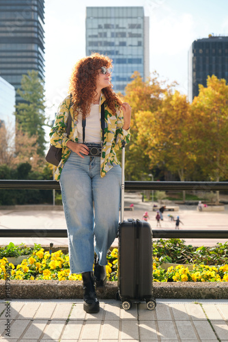 Tourist looking at cityscape while waiting with suitcase and camera photo