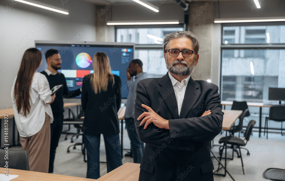 Handsome senior man is posing. Group of office workers are indoors together Handsome senior man is posing. Group of office workers are indoors together