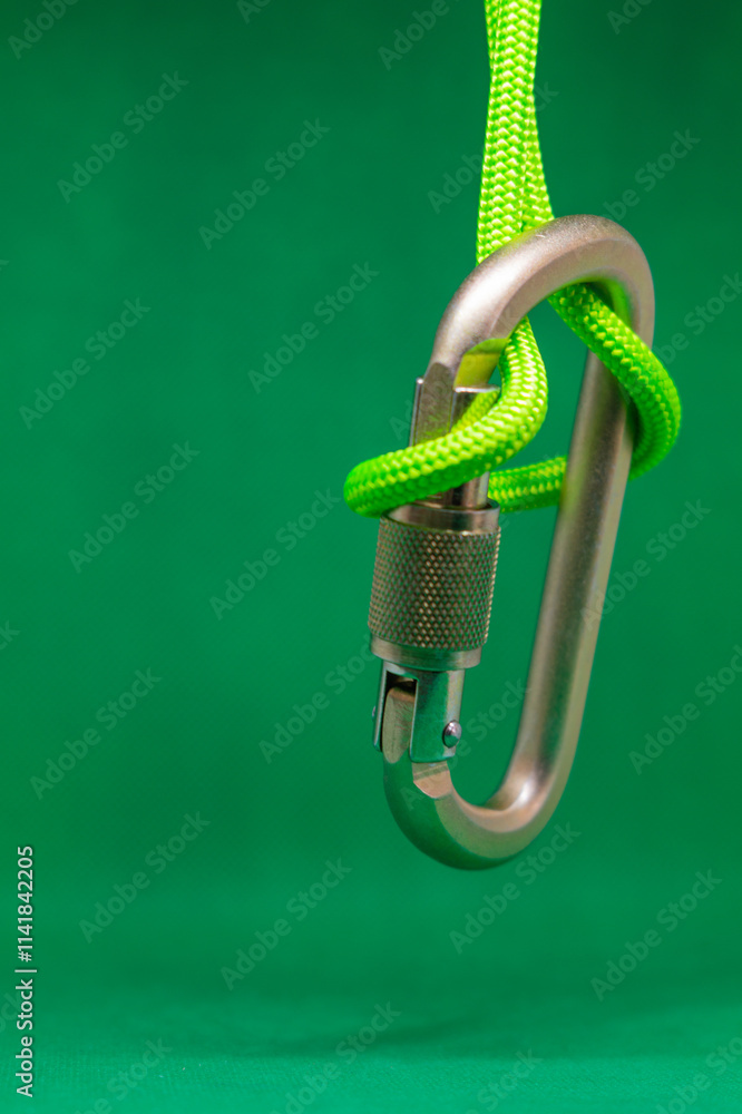 Obraz premium Metal climbing carabiner hanging on rope on green background, side view