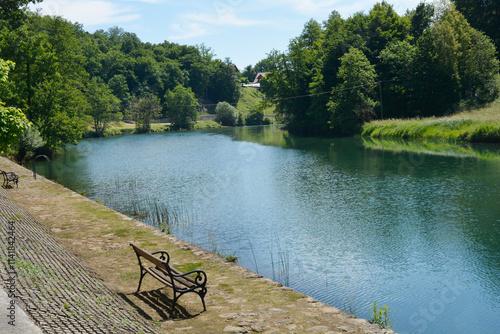 Fototapeta Naklejka Na Ścianę i Meble -  North stone shore of the Dobra River with benches near the village of Jarce Polje in Croatia