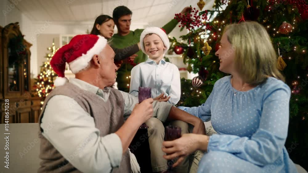 Warm family atmosphere in Christmas vacation, portrait of boy and grandparents. Cheerful little child and senior man and woman sitting on sofa in living room, parents decorating Xmas tree, happiness Warm family atmosphere in Christmas vacation, portrait of boy and grandparents. Cheerful little child and senior man and woman sitting on sofa in living room, parents decorating Xmas tree, happiness