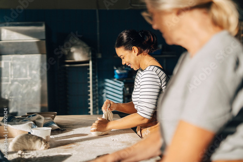 Smiling female baker kneading dough with senior colleague while working at bakery
