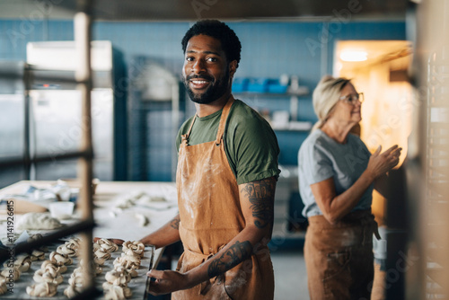 Portrait of smiling male baker holding tray of fresh cinnamon buns while standing in bakery photo