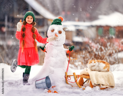 Obraz na płótnie Kid girl makes snowman on winter frosty day. Child makes nose out of carrot. Outdoor family fun on Christmas vacation in the winter new year w salonie