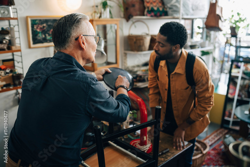 Senior male owner explaining lamp features to customer at antique store photo