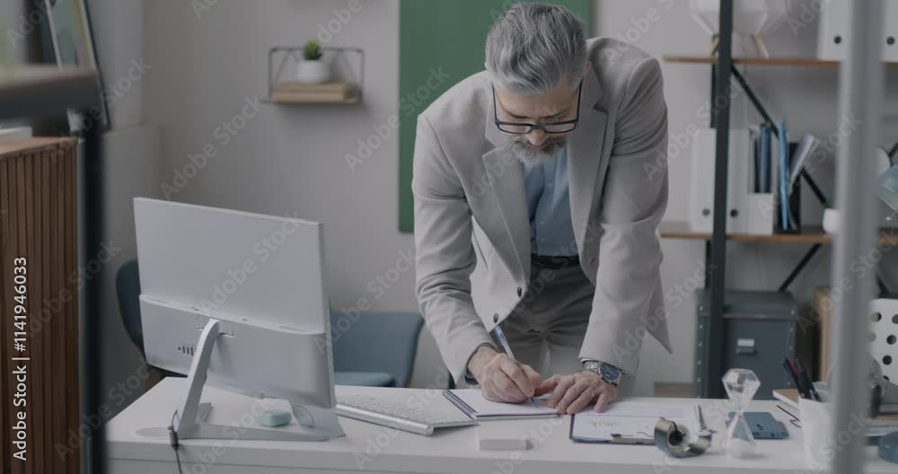 Experienced businessman working in office writing in notebook looking at computer monitor. Professional occupation and businessperson concept. Experienced businessman working in office writing in notebook looking at computer monitor. Professional occupation and businessperson concept.