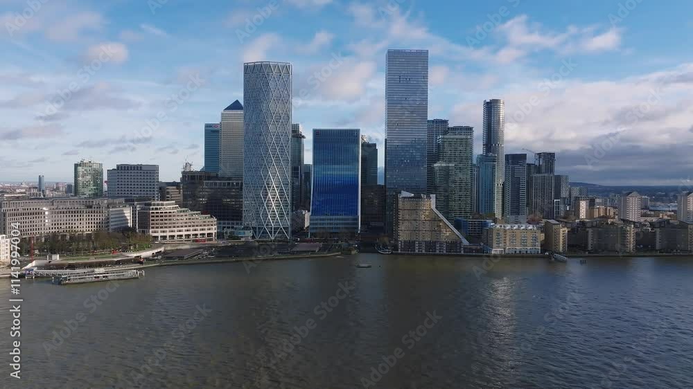 Aerial perspective of Canary Wharf's modern skyscrapers, including One Canada Square, with the Thames River in the foreground under a partly cloudy sky. Aerial perspective of Canary Wharf's modern skyscrapers, including One Canada Square, with the Thames River in the foreground under a partly cloudy sky.