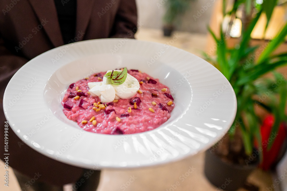 A beautifully presented plate of vibrant pink beetroot risotto topped with poached eggs and sprinkled with pine nuts, served in a stylish setting with greenery in the background. A beautifully presented plate of vibrant pink beetroot risotto topped with poached eggs and sprinkled with pine nuts, served in a stylish setting with greenery in the background.