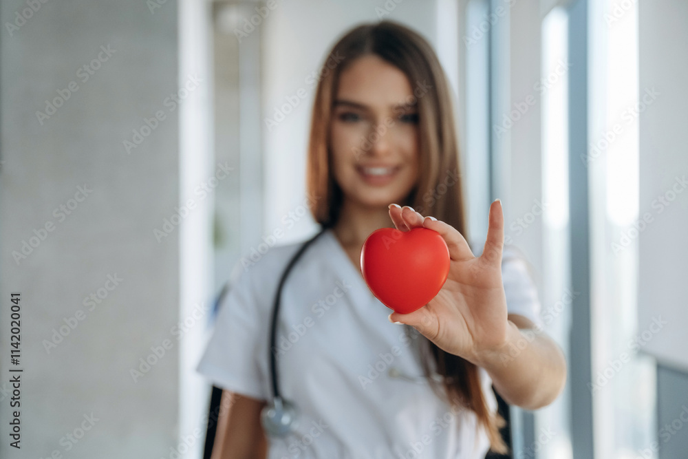 Little red heart in hands. Professional female doctor in the clinic indoors Little red heart in hands. Professional female doctor in the clinic indoors