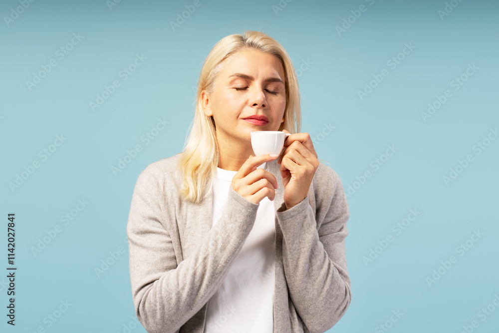 Senior woman enjoying the aroma of coffee with closed eyes on blue background Senior woman enjoying the aroma of coffee with closed eyes on blue background