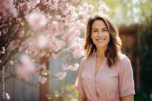 Portrait of a beautiful mature woman in pink dress standing in front of a blooming cherry tree