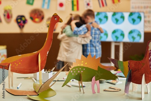 Close up background image of colorful handmade dinosaur figures painted during art and craft class with group of kids hugging in background copy space photo