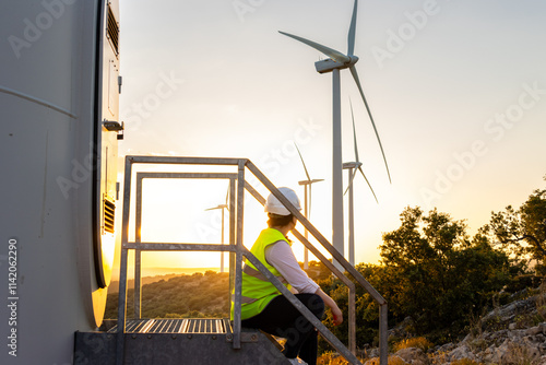 Female engineer resting on wind turbine stairs at a wind farm during sunset photo