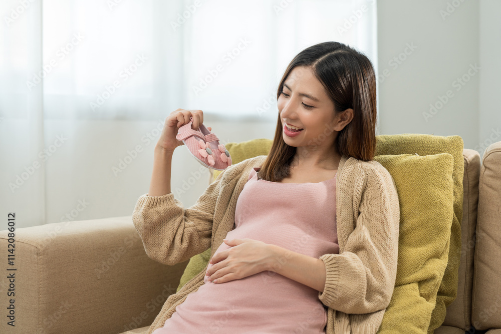 Happy pregnant woman looking at tiny kids pink shoes while caressing her belly at home, happy motherhood waiting for childbirth, family planning and pregnancy with insurance for child health. Happy pregnant woman looking at tiny kids pink shoes while caressing her belly at home, happy motherhood waiting for childbirth, family planning and pregnancy with insurance for child health.