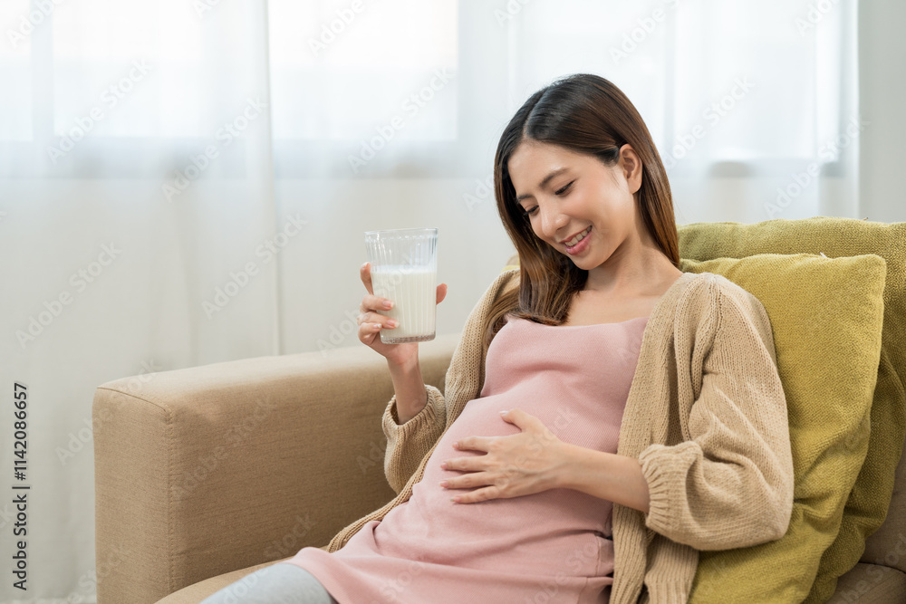 Happy pregnant woman drinking milk and caressing her belly while sitting on sofa at home, concept of healthy mother taking health care and nourish her fetal and waiting her childbirth. Happy pregnant woman drinking milk and caressing her belly while sitting on sofa at home, concept of healthy mother taking health care and nourish her fetal and waiting her childbirth.